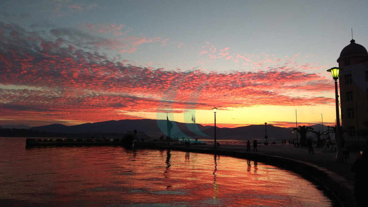 Roter Sonnenuntergang über der Uferpromenade und dem Hafenbecken von Volos